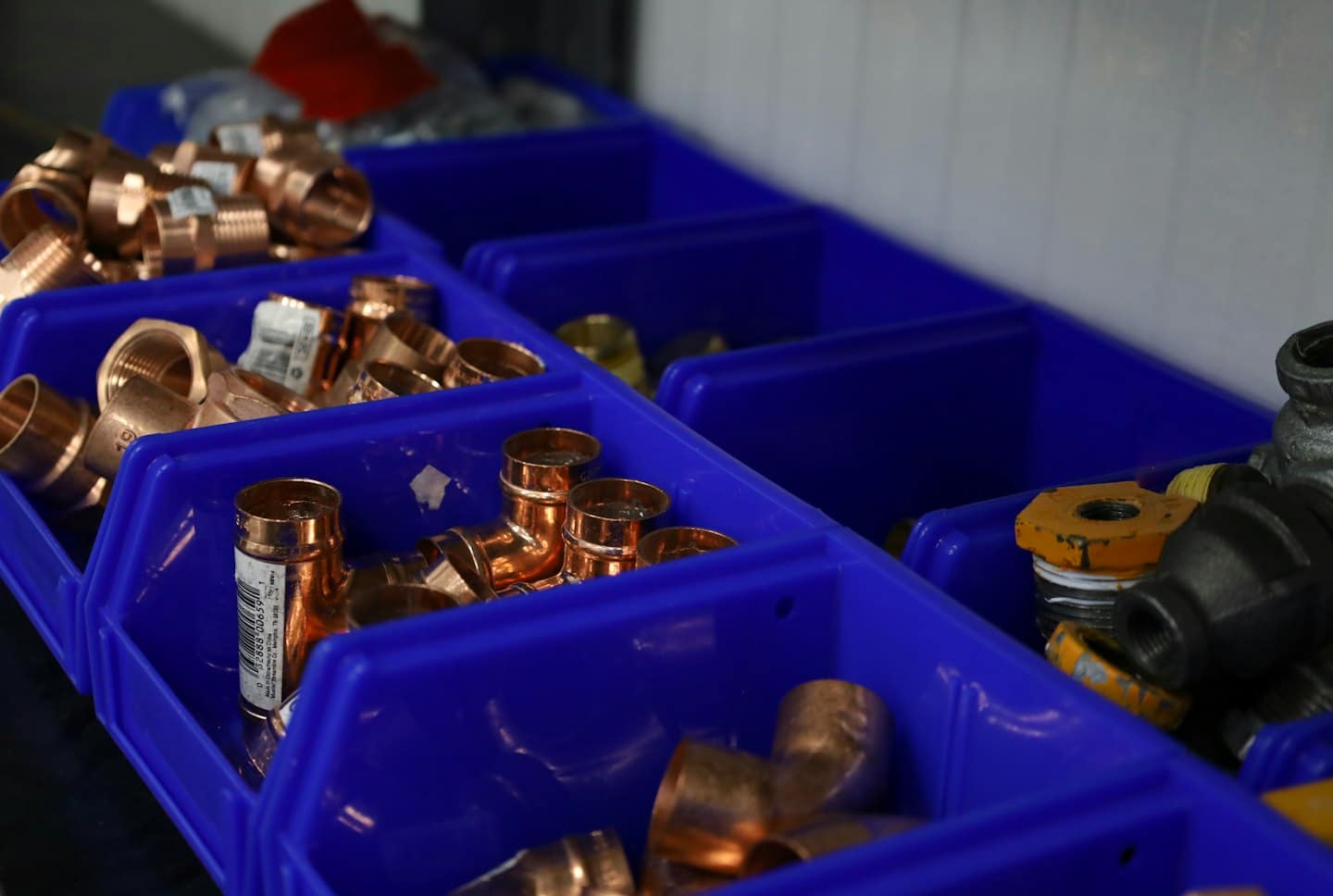 Różne miedziane i żelazne złączki hydrauliczne ułożone w niebieskich pojemnikach.